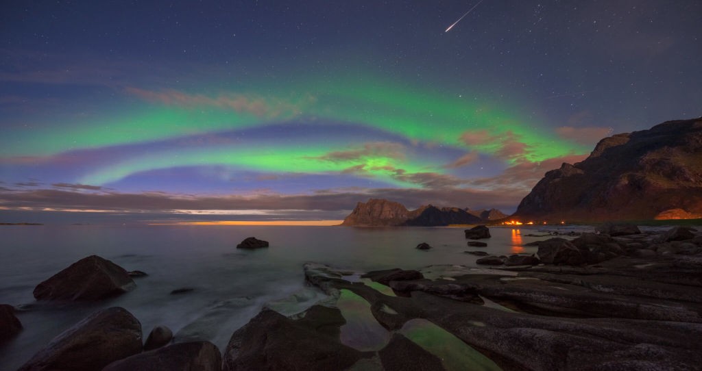 Aurora Borealis at twilight over a beach in norway, with a shooting star in the sky