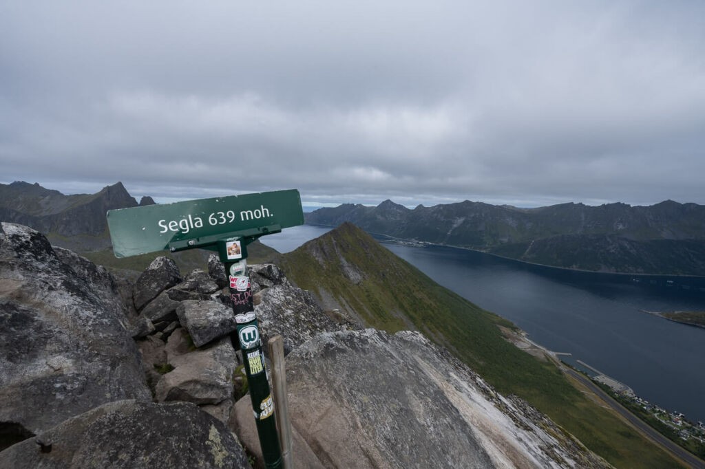 Signpost on top of the Segla mountain with the fjords and other mountains in the background