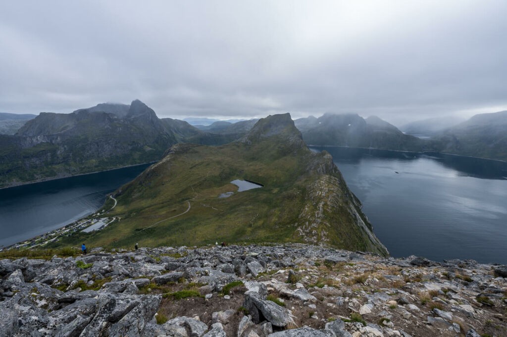 Hikers on the trail to the top of the segla mountain with fjords and steep mountain in the background.