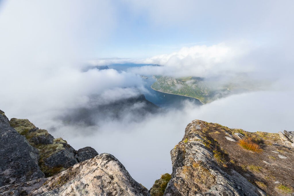 View from the top of Grytetyppen over a fjord surrounded by clouds on a sunny day.