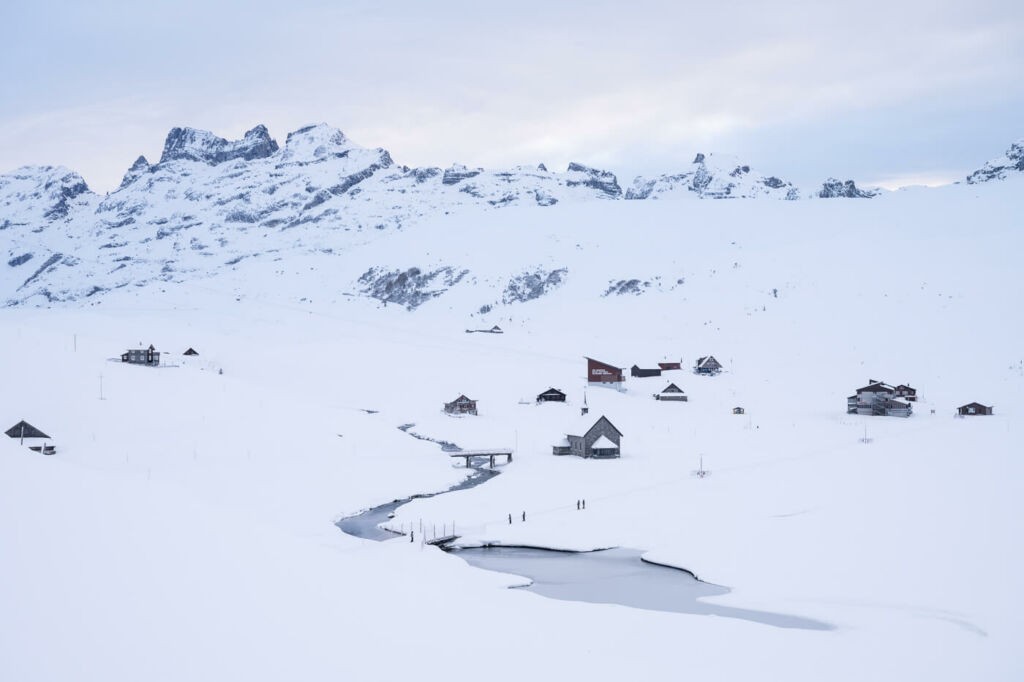 A few huts and a Chapelle covered in snow on a plateau high in the alps.