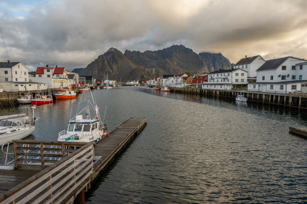 The Henningsværr town center with row of houses around a canal and a mountain in ht e background