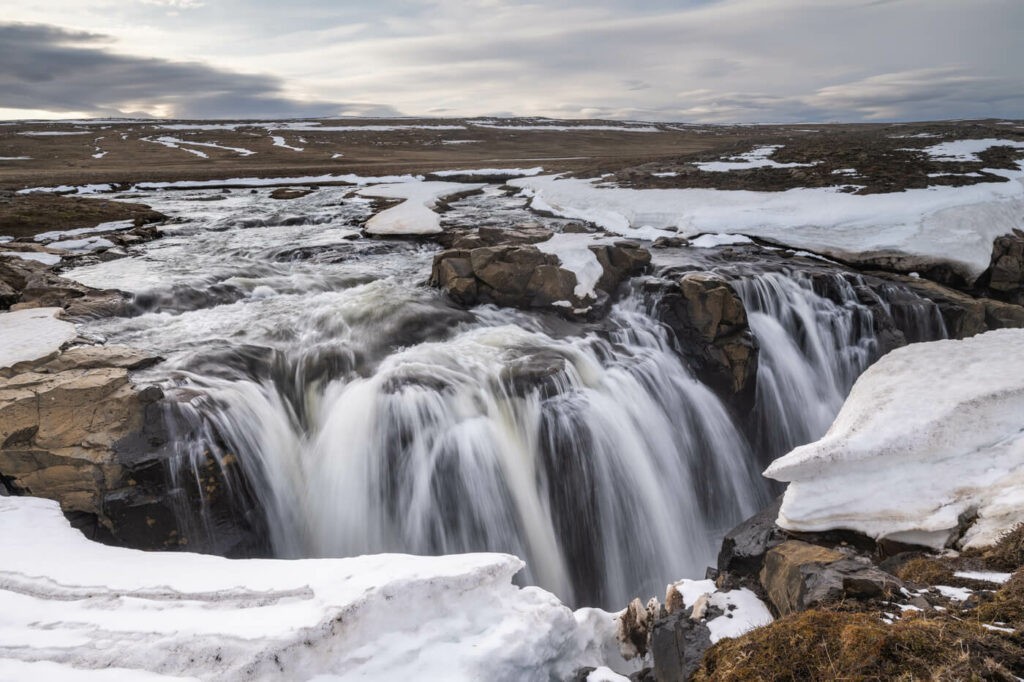 The first waterfall on the waterfall circle hike in Laugarfell, surrounded by snow in the landscape.