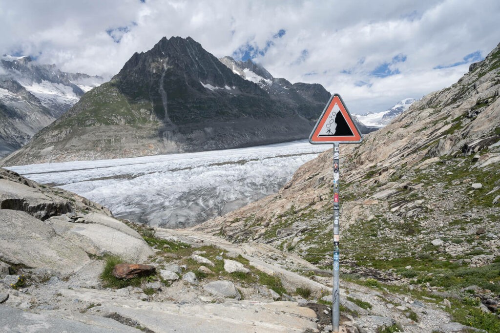 Alpine landscape with a glacier in the background and a rockfall warning sign in the foreground.