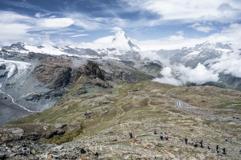 Hikers looking at the alpine landscape around the Matterhorn, during a hike from Zermatt to the summit of the Gornergrat via the Riffelsee.