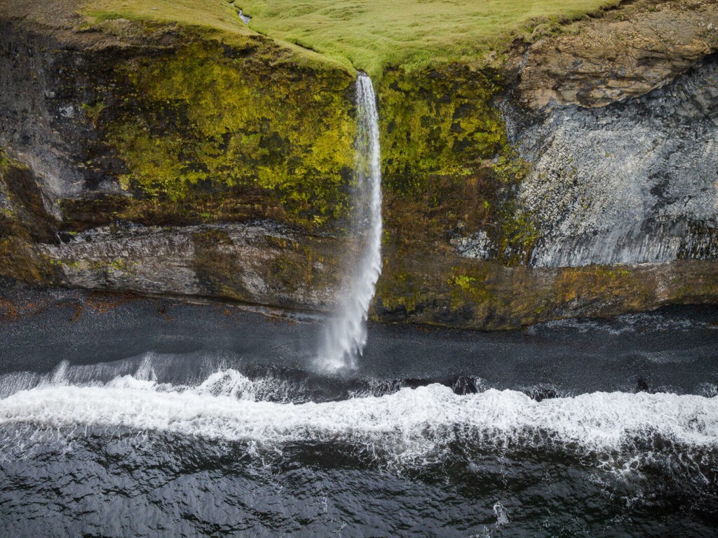 Ketubjorg waterfall falling from the cliffs on a black sand beach