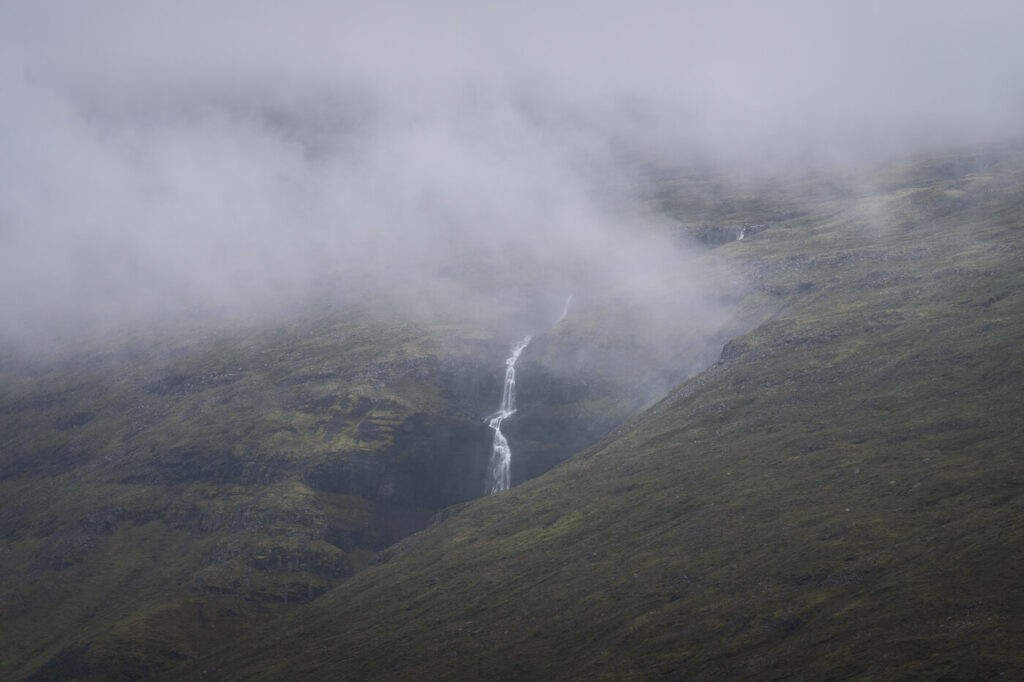 Dark image of a waterfall in the Strutsgil canyon, surrounded by clouds on a foggy day.