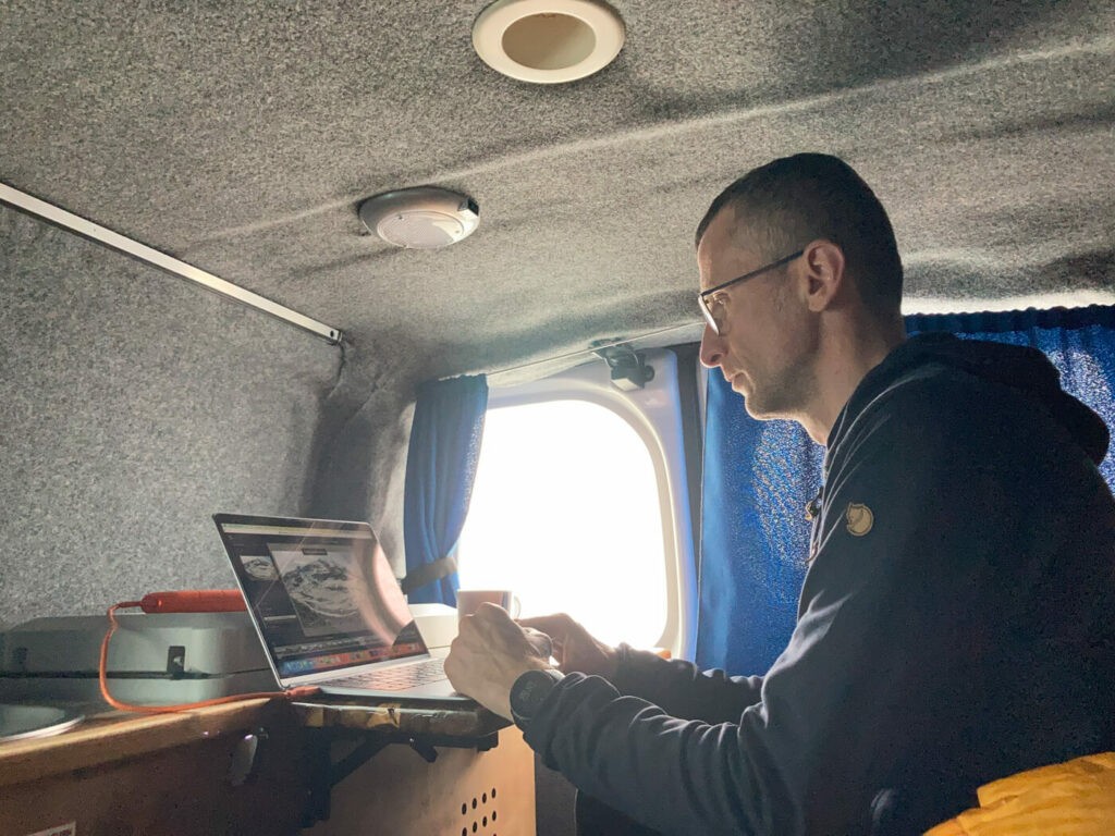 A person working on a laptop in a caddy easy small campervan from camp easy during a ring road trip in iceland.