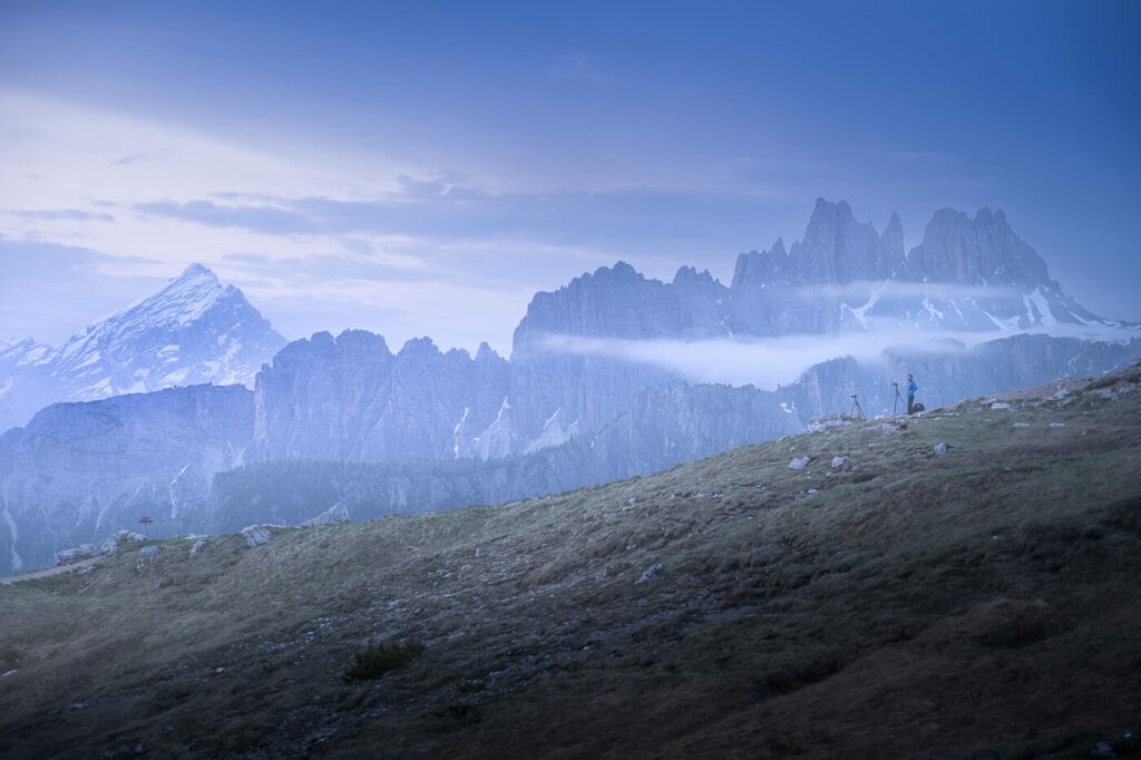 A hiker doing landscape photography waiting for sunrise in the dolomites during blue hour.