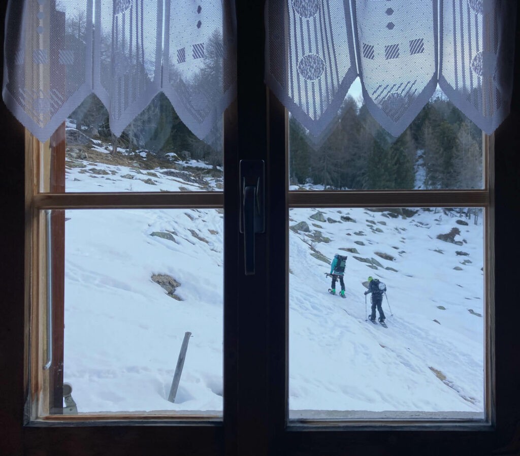 Cross country skiers viewed through a window in Rifugio Saoseo
