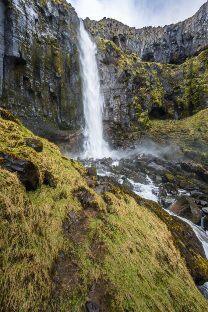 Vertical photo of Grundarfoss, a waterfall framed by black basalt columns in Iceland.