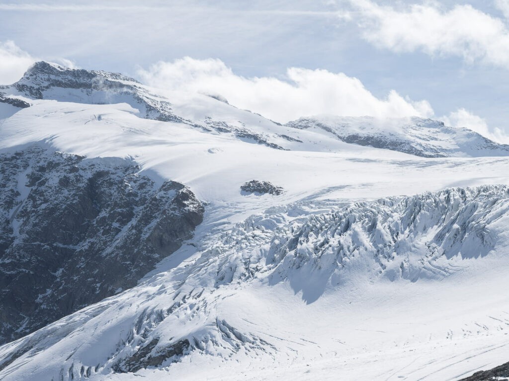 mountains covered in snow and ice above, with several visible crevasses of a glacier'